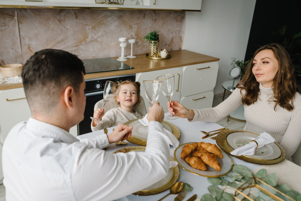 早餐。年轻的一家三口在家里一起吃早餐。爸爸，妈妈和可爱的小孩吃着羊角面包，谈笑风生。一对夫妇带着女儿在厨房。图片下载