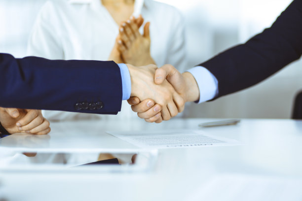 商务人士在会议或谈判中握手，特写。一群不知名的商人，背景是一个女人在一间现代化的办公室里。团队合作，伙伴关系和握手的概念图片下载