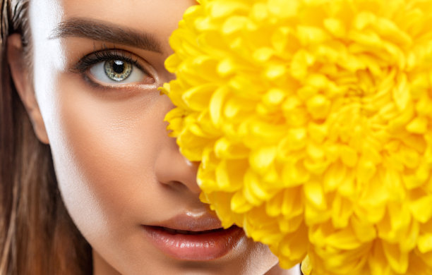 这是一个有着健康干净皮肤和美丽妆容的迷人女孩的肖像，她手里拿着一朵黄色的菊花。美学美容和化妆概念。图片下载