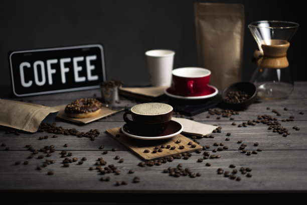 一张旧木桌上的咖啡照片。桌子上有咖啡杯、咖啡豆、甜甜圈、咖啡袋、Chemex过滤咖啡和一个盘子。图片下载