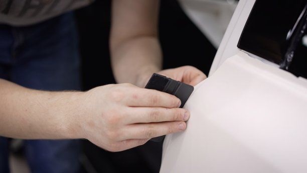 师傅在车身上涂了一层白色保护膜。汽车维修工人在汽车装饰车间给车身涂防重力膜。汽车保养，师傅用文员刀在车上剪下胶片。图片下载