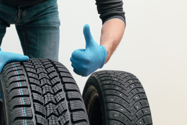 更换冬季和夏季轮胎。白色背景下，机修工拿着轮胎。冬季铆钉轮胎，更换轮胎图片下载