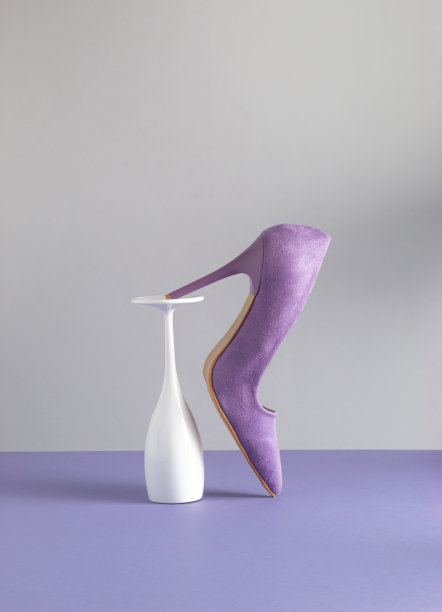 柔和的紫色优雅的女士高跟鞋和白色香槟酒杯在紫色的背景。最小的派对创意与复制空间。图片下载