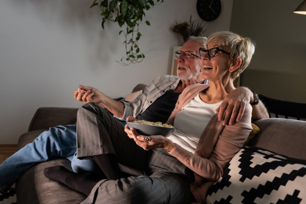 老夫妇坐在沙发上吃爆米花。他们在看电影。图片下载