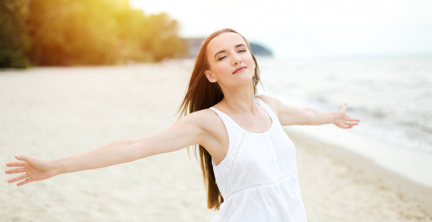 快乐的微笑的女人在自由的幸福幸福的海洋海滩站着，张开双手。一个多元文化的女模特的肖像，穿着白色的夏装，在旅游假期享受大自然图片下载