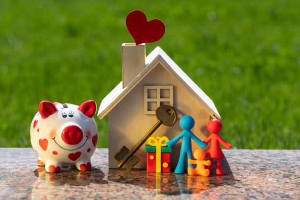 一个具有象征意义的家庭的小雕像，一个木制的微型房子和一个以草为背景的储蓄罐图片下载