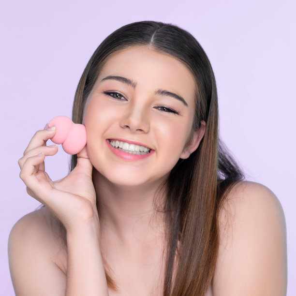 年轻迷人的女孩在脸上涂抹粉底的肖像。图片下载