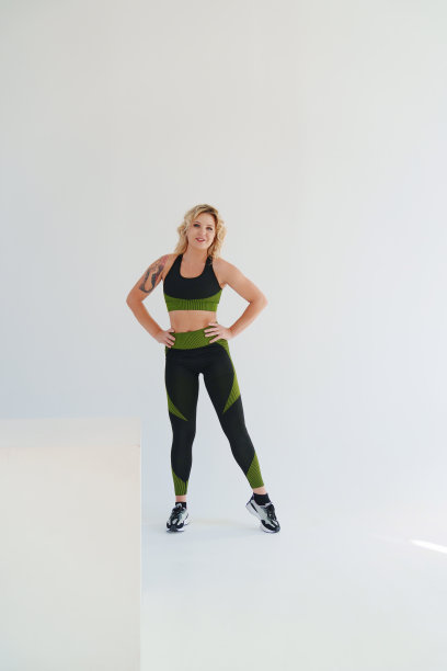 一位身穿黑绿运动服的迷人金发女郎在白色背景上摆姿势。图片下载
