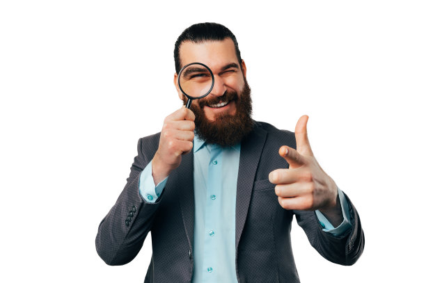 大胡子男子正透过放大镜看着镜头。图片下载