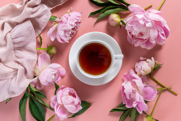 女性化的花卉构图。一杯茶和粉红色的牡丹花在粉红色的背景。平躺，俯视图。图片下载