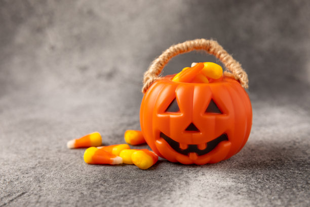 万圣节南瓜南瓜灯桶和玉米糖庆祝万圣节。经典的白色，橙色和黄色棒棒糖南瓜软糖在黑色的背景。副本的空间。放文字的地方。图片下载