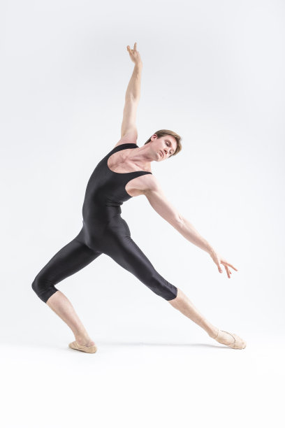 专业芭蕾舞演员年轻的白人运动员穿着黑色西装在白色的工作室摆姿势伸展双手。图片下载