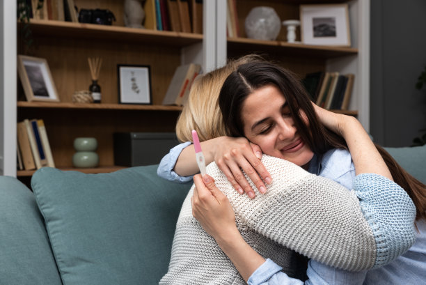 一名拿着验孕棒的年轻女子喜出望外地告诉她的妈妈，她怀孕了，将要生孩子了。未来的奶奶和妈妈开心地坐在家里的沙发上图片下载