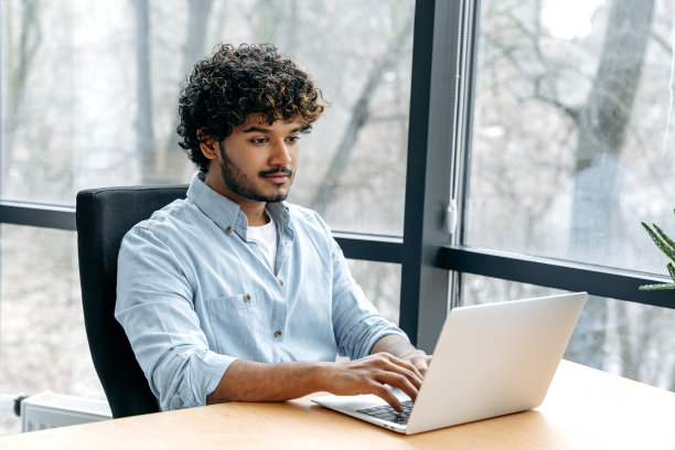 聪明成功自信的印度或阿拉伯人，公司seo, IT专家，人力资源经理，坐在办公室的办公桌前用笔记本电脑工作，看着笔记本电脑屏幕，微笑图片下载