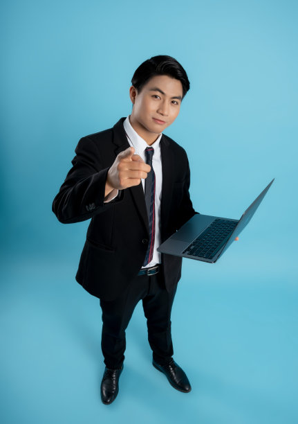 年轻商人在蓝色背景下使用笔记本电脑的肖像图片下载