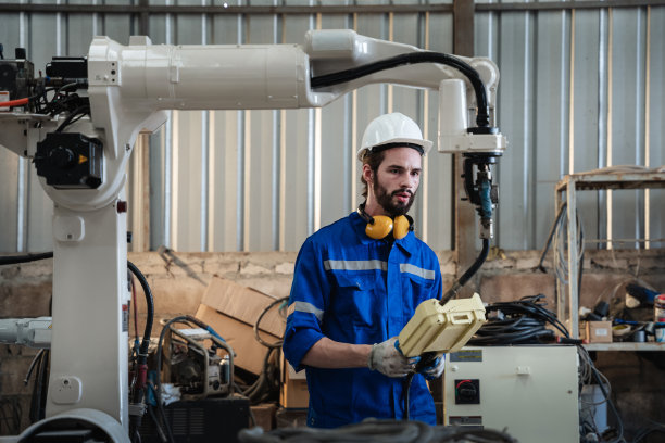 工业工程师在工业制造工厂中控制自动机械臂、焊接机、焊接机器人。图片下载