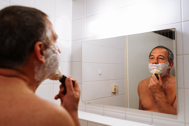 中年男子赤裸上身，看着镜子里的自己，用剃刀刮着脸图片下载