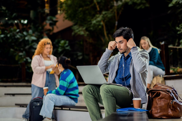 男生坐在校园里使用笔记本电脑的照片。图片下载