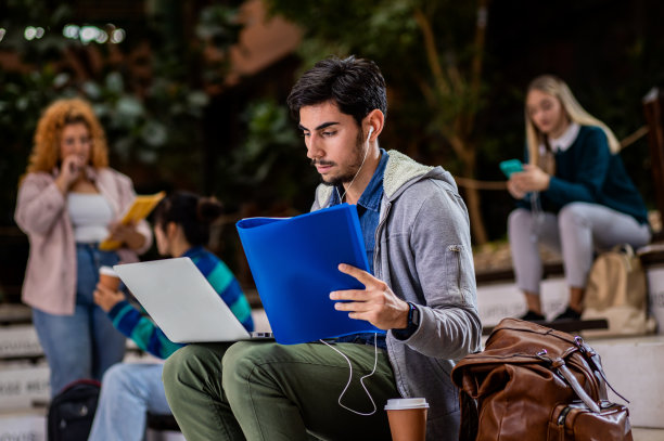 男生坐在校园里使用笔记本电脑的照片。图片下载