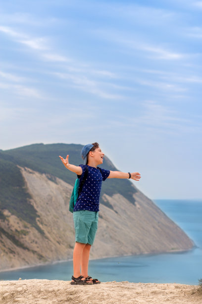 一个背着背包的男孩在山顶上张开双臂，唱着喜悦和旅行印象的歌。积极的情绪，灵魂音乐。图片下载