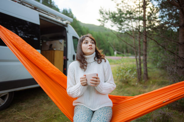 一名妇女在露营车附近的吊床上休息时喝茶图片下载