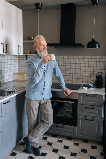 沉思的成熟老年男性早上在家里喝热咖啡，透过窗户看。老人在喝茶图片下载
