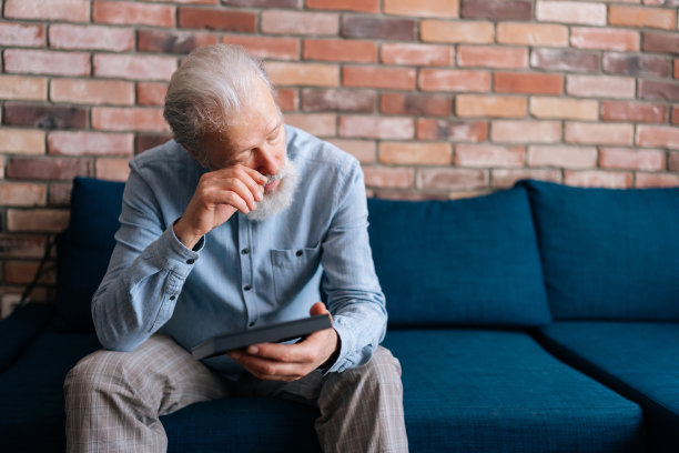 悲伤的灰色头发的成年男子坐在家里的沙发上，看着相框里妻子的照片哭泣。概念怀旧，悲伤图片下载