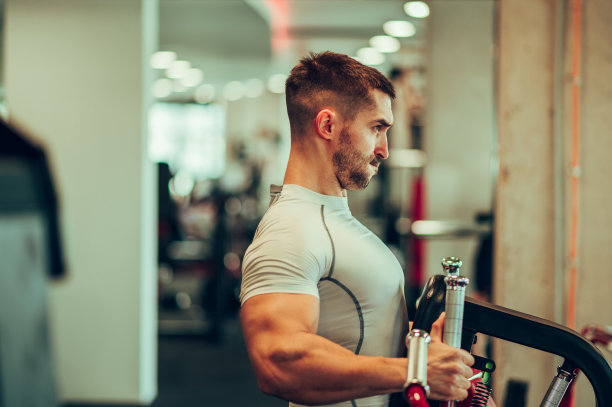 健身房里，一个肌肉发达的运动员穿着运动服在拉胸机前的侧视图。图片下载