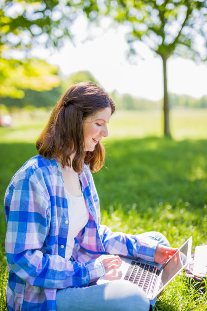 一个漂亮女人拿着笔记本电脑坐在公园的草地上图片下载