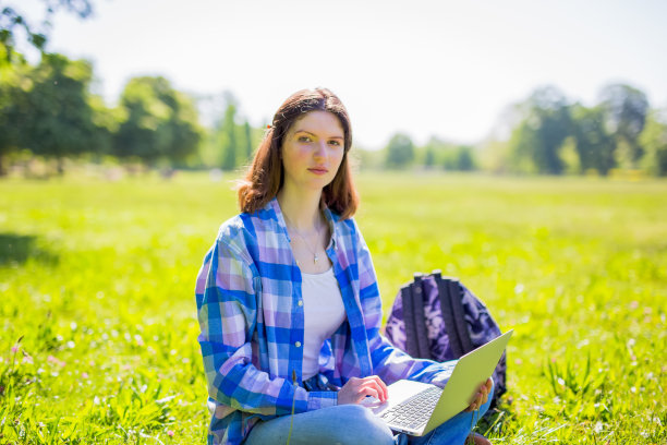 一个漂亮女人拿着笔记本电脑坐在公园的草地上图片下载