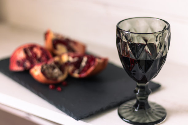 桌上的石榴配上一杯酒。石榴籽和红酒切块。水果和酒。夏日静物。酒精饮料和多汁成熟的石榴。夏天的维生素。图片下载