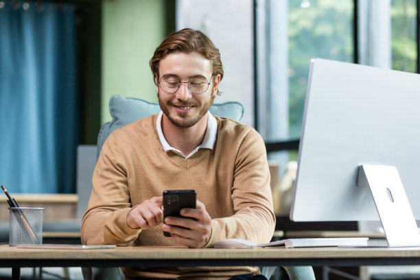 一个年轻的自由职业者，程序员在家工作。坐在办公桌前，用电话，写信息，查邮件图片下载