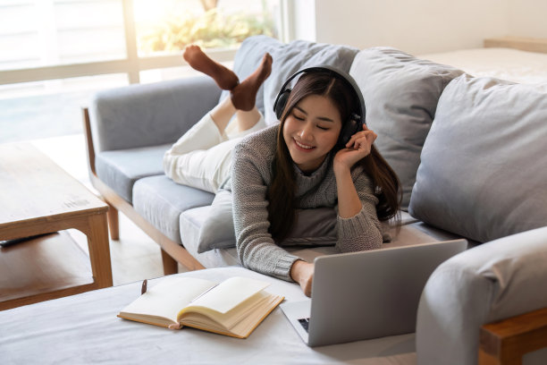 年轻女子躺在沙发上，听着音乐，闭着眼睛放松图片下载