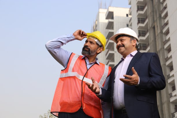 快乐的印度建筑经理与建筑工程师交谈。站在楼前讨论。欢呼起来。图片下载