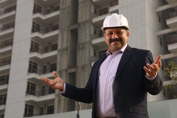 一个快乐的印度建筑工人戴着建筑工人的头盔站在一个建筑商的财产前。图片下载