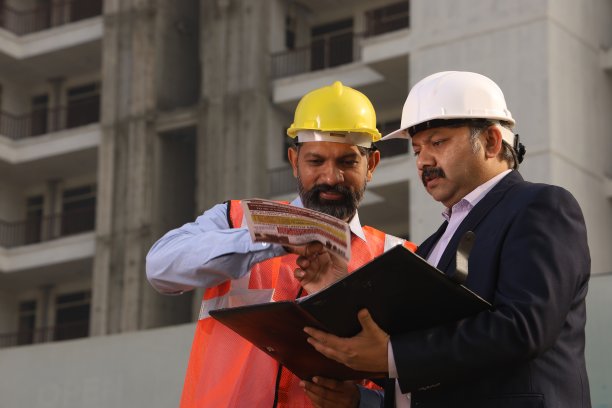 快乐的印度建筑经理与建筑工程师交谈。站在楼前讨论。查看文件和报告。图片下载