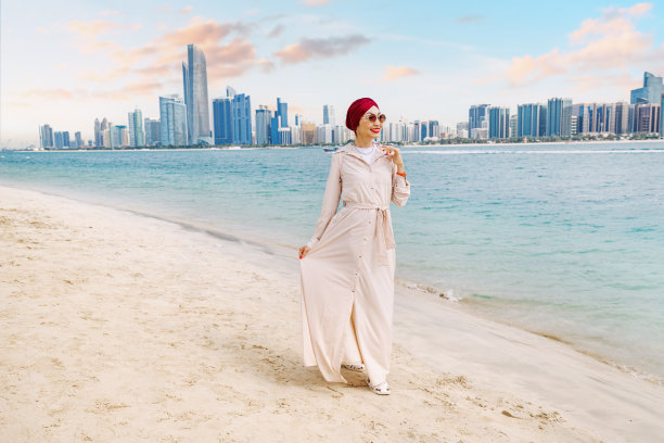 年轻印度女子走在海滩上，欣赏阿布扎比高耸摩天大楼的壮丽海景图片下载
