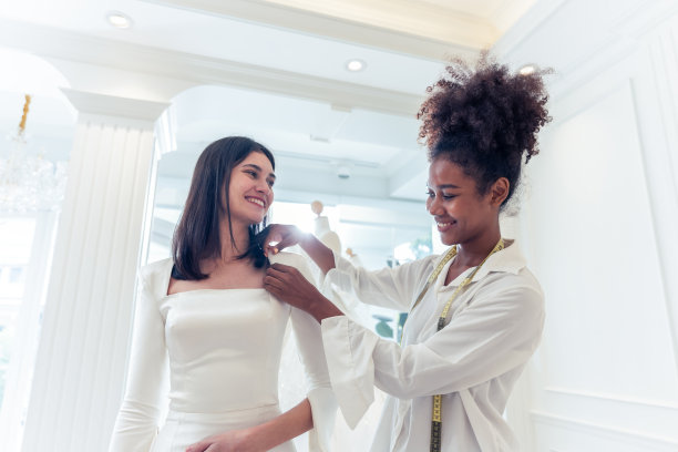 美丽的新娘在工作室与婚礼策划师讨论细节。有吸引力的婚纱店老板设计师妇女帮助和支持顾客选择婚纱在商店。婚礼仪式概念。图片下载