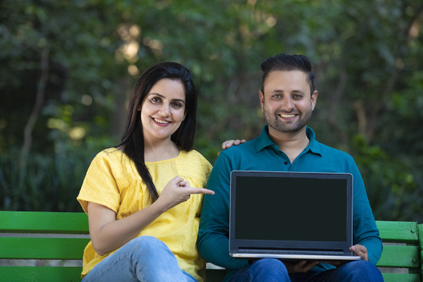 年轻的印度夫妇在公园展示笔记本电脑屏幕。图片下载