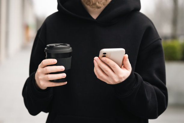 一个男人手里的可重复使用的时尚黑色竹杯和智能手机(特写)。图片下载
