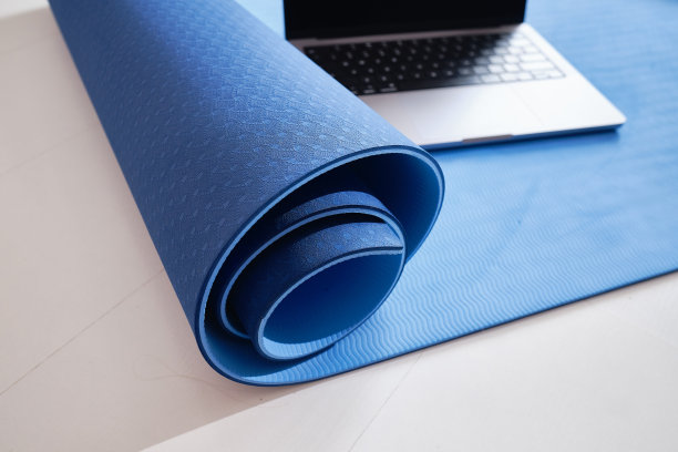 在笔记本电脑上进行在线锻炼的概念以及健康的生活方式和健身。瑜伽垫和笔记本电脑在浅色背景下的特写。在家锻炼图片下载
