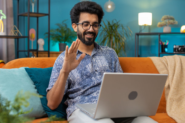 男人坐在家里的沙发上，看着摄像头，与朋友或家人进行视频会议图片下载