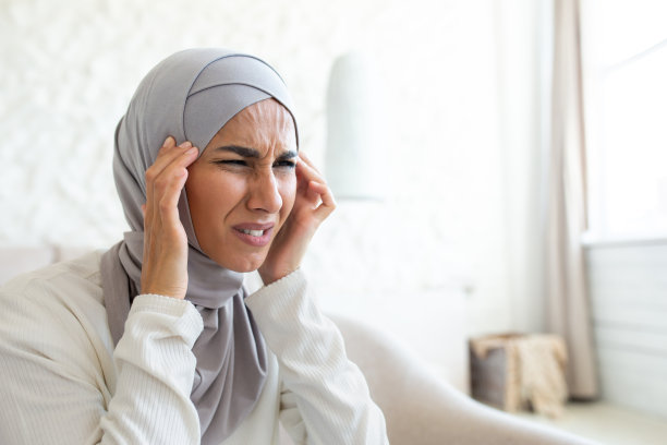 一位戴着头巾的年轻女人双手抱头，感到剧烈疼痛，按摩自己，因紧张而面部扭曲的特写照片图片下载