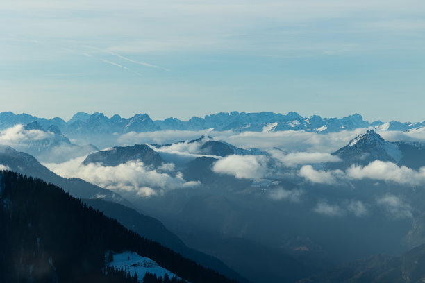 从高山上的一个自然的山地环境的近距离观察，从侧面照射在下午的阳光，在冬季。轻云在白雪皑皑的山峰间穿梭图片下载