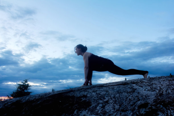 年轻女子在岩石地区的夕阳下练习瑜伽图片下载