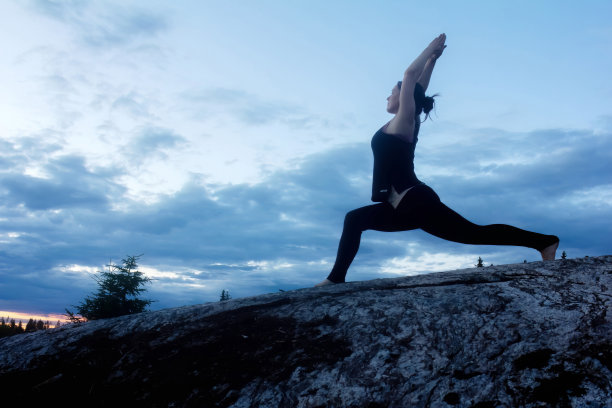 年轻女子在岩石地区的夕阳下练习瑜伽图片下载
