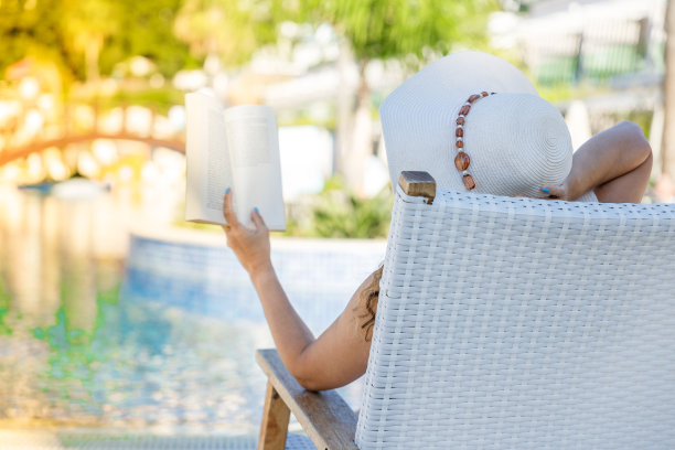 年轻女子在游泳池附近的躺椅上看书图片下载