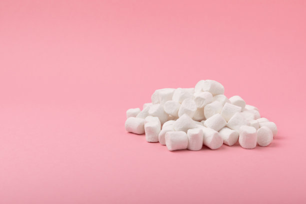 粉红色背景上的松散棉花糖。白色的棉花糖平铺。甜食和零食当零食。咀嚼糖果的特写。副本的空间。放文字的地方。冬季食物概念。图片下载