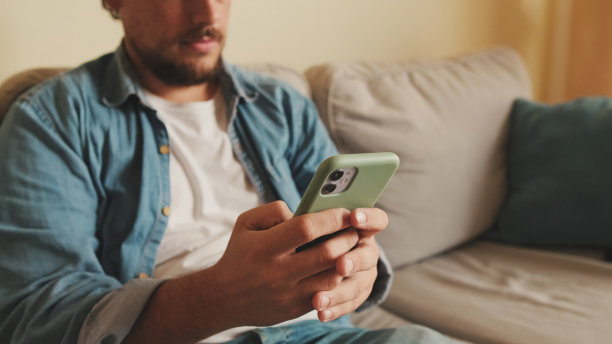 客厅沙发上，一个面带微笑的家伙拿着手机的特写图片下载