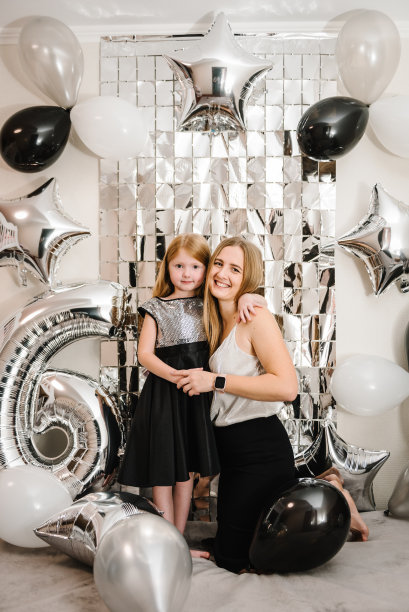 妈妈在女儿将近一岁的时候祝贺她生日。幸福的家庭庆祝6年生日聚会。母亲抱着孩子。照片墙装饰白色、黑色、银色气球。在一起很开心。图片下载